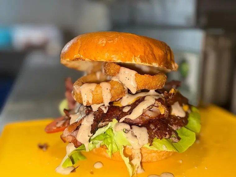 Smash burger con doppia carne, anelli di cipolla, bacon e salsa bianca, sul bancone del locale