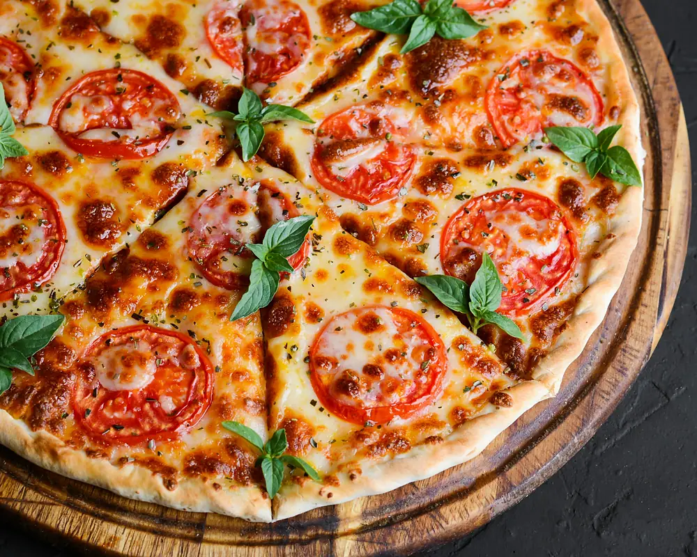 Pizza tonda con pomodoro a fette, mozzarella e basilico (immagine illustrativa)